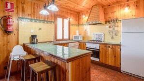 Eine Holz-Küche mit Fliesenrückwand, Holz-Barhocker, einer Mikrowelle, einem Herd und einem weißen Kühlschrank.
