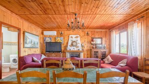 Ein Holzblockhaus-Interieur mit Esstisch, Stühlen, einer Couch, einer Pendelleuchte und einem Kamin.