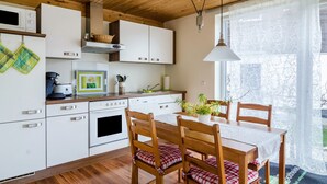 Cozinha moderna com armários brancos, teto de madeira e área de jantar com mesa e cadeiras.