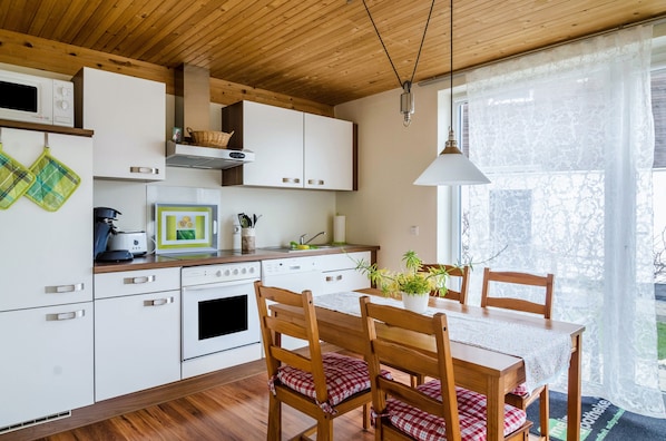 Une cuisine moderne avec des meubles blancs, un plafond en bois et un coin repas comprenant une table et des chaises.
