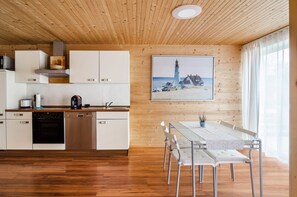 Una cocina moderna con armarios de madera, un comedor con mesa y sillas, y un cuadro de un faro en la pared.