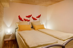 Una cama doble con dos almohadas, una mesita de noche con una lámpara, y una pared decorada con motivos florales rojos.