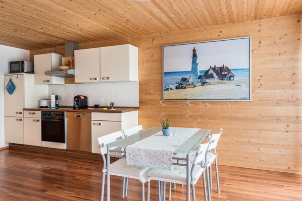 Una cocina moderna con armarios blancos, un microondas y una estufa. Hay un comedor con una mesa y sillas, y un cuadro de un faro en la pared.