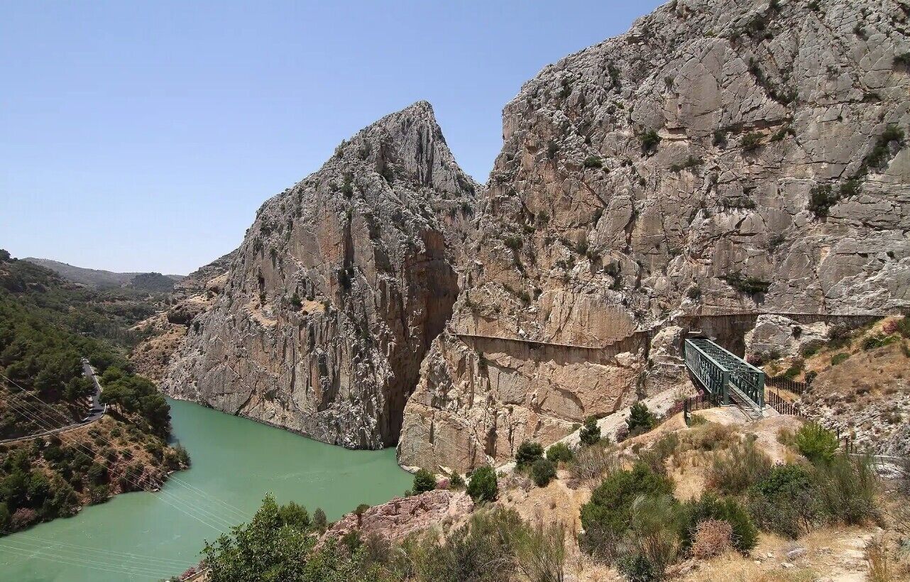 Un cañón rocoso con un río, un puente y un pequeño edificio.