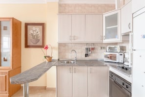 A modern kitchen with a granite countertop, stainless steel sink, white cabinets, a microwave, a toaster, and a dishwasher.