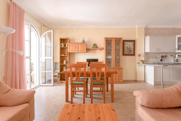 A living room with a sofa, a wooden table, and a kitchen area with cabinets and a countertop.
