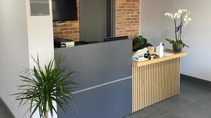 Een receptiebalie met een bakstenen muur op de achtergrond, een flatscreen-tv en een potplant.