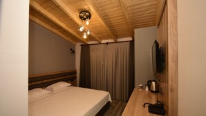 Een slaapkamer met een houten plafond, een bed met witte beddengoed, een houten bureau met een waterkoker en een afstandsbediening, en een televisie aan de muur bevestigd.