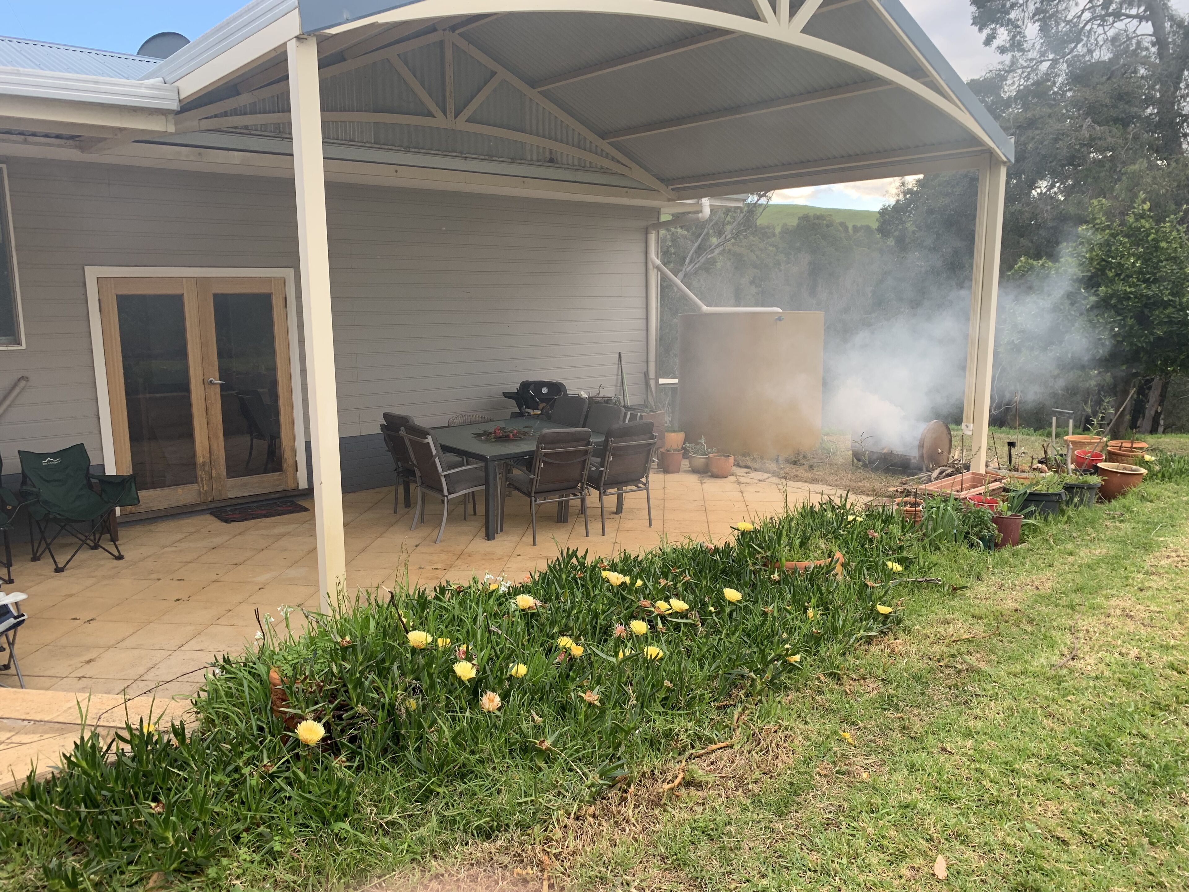Un porxo cobert amb taula i cadires, una barbacoa i plantes en testos.