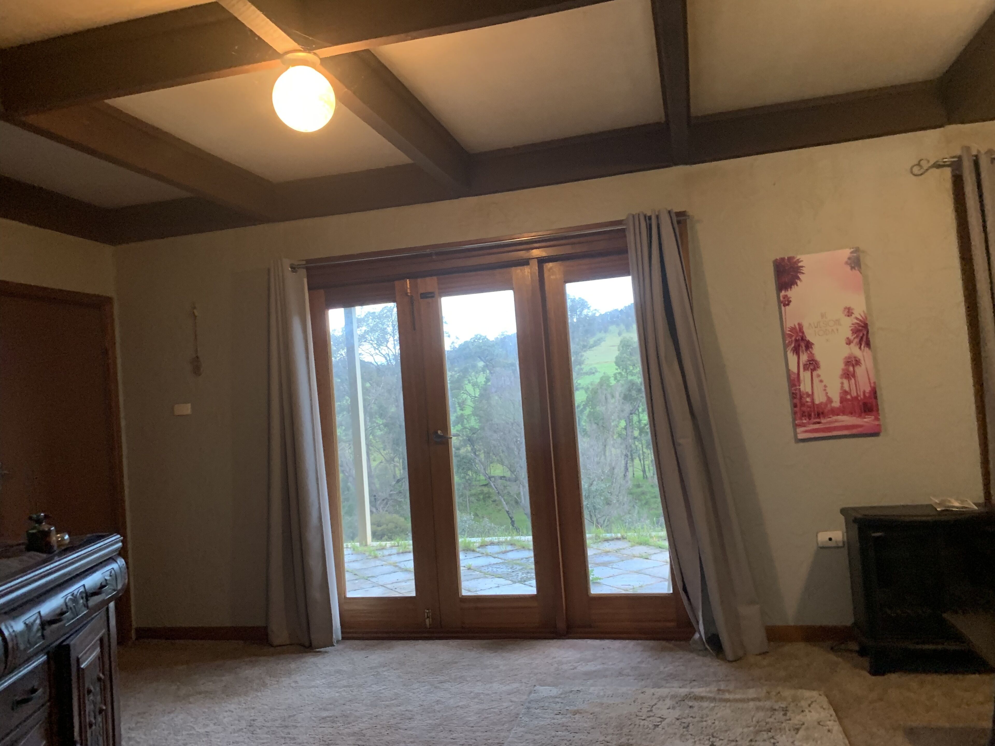 A room with a large sliding glass door leading to a garden, a wooden dresser, and a small table with a lamp.