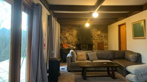 A cozy living room with a stone fireplace, leather sofa, and a large window with curtains.
