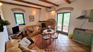 A cozy living room with a sofa, a dining table with chairs, a fireplace, and a kitchen area with cabinets. - Apartment Andrea (Poreč)