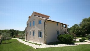 A two-story house with a tiled roof, a stone facade, and a well-maintained lawn. - Apartment Andrea (Poreč)