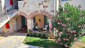 A stone building with a staircase, a small outdoor seating area, and a garden with pink flowers. - Apartment Andrea (Poreč)