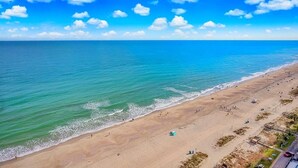 Een strand met helderblauw water, een zandstrand en enkele mensen.