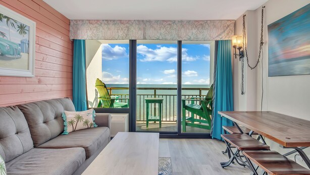 Een kamer met een bank, een tafel en een balkon met uitzicht op zee.