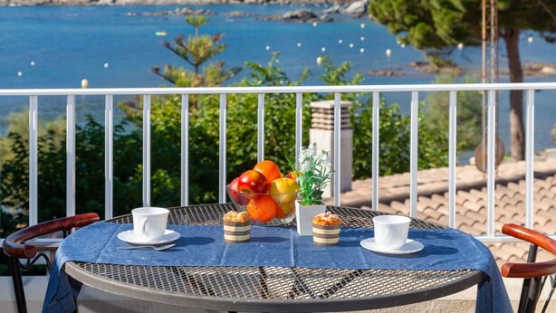 A table with a view of a coastal town, a bowl of fruit, and two cups on a balcony. - Stunning  villa for 6 people with WIFI, TV, patio, pets allowed and panoramic view (Llançà)