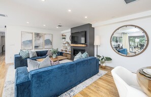 A modern living room with a blue sofa, a flat-screen TV, and a round mirror. - Lakefront Haven - Downtown Kelowna!   (Kelowna)