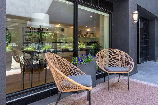 Deux fauteuils en osier avec des coussins, placés à l’extérieur d’un bâtiment doté de grandes fenêtres.