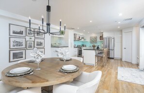 Une cuisine moderne avec des meubles blancs, un réfrigérateur en acier inoxydable et un coin repas comprenant une table ronde et des chaises blanches.