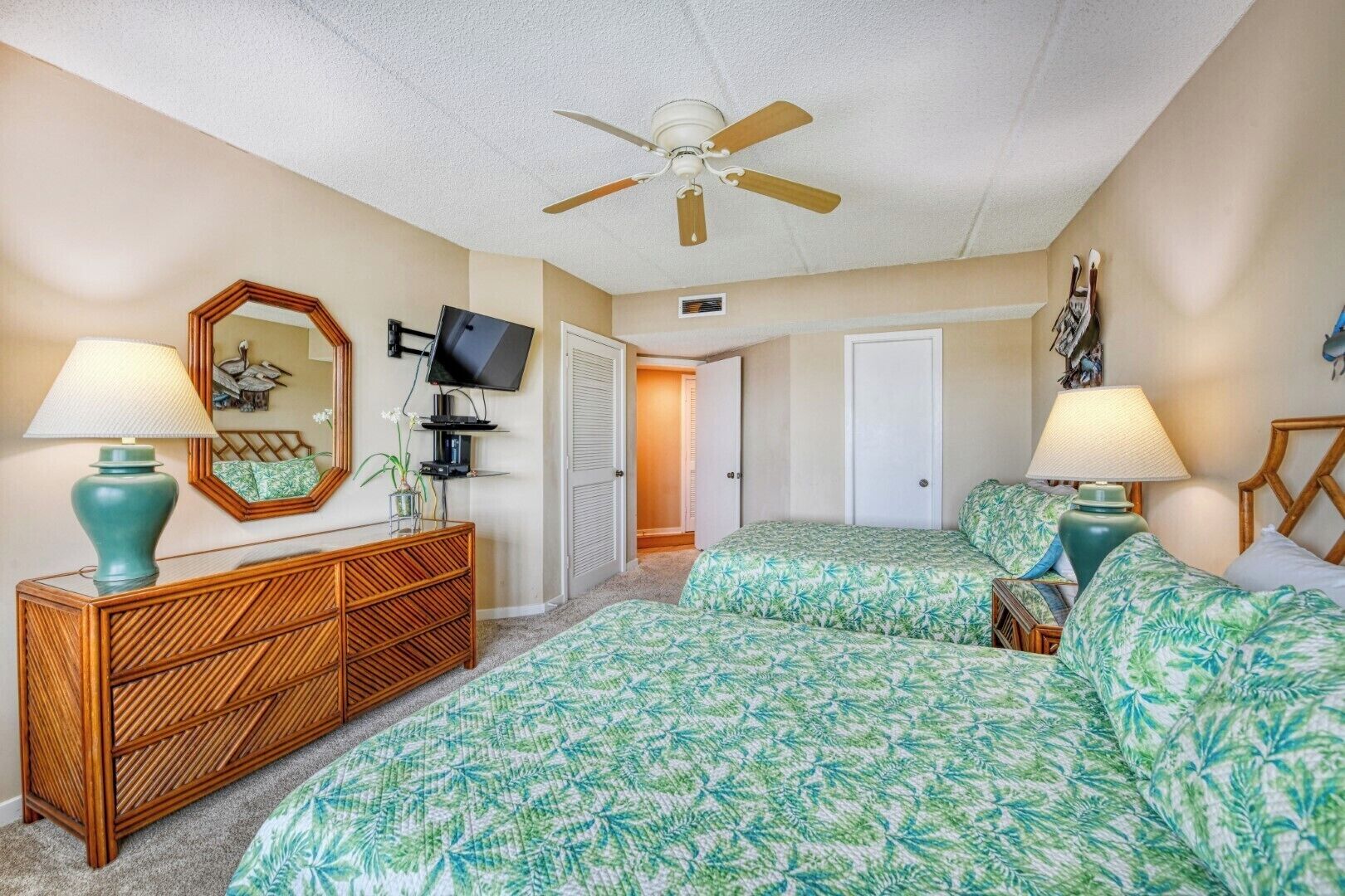 A bedroom with two beds, a ceiling fan, a TV, and a dresser.