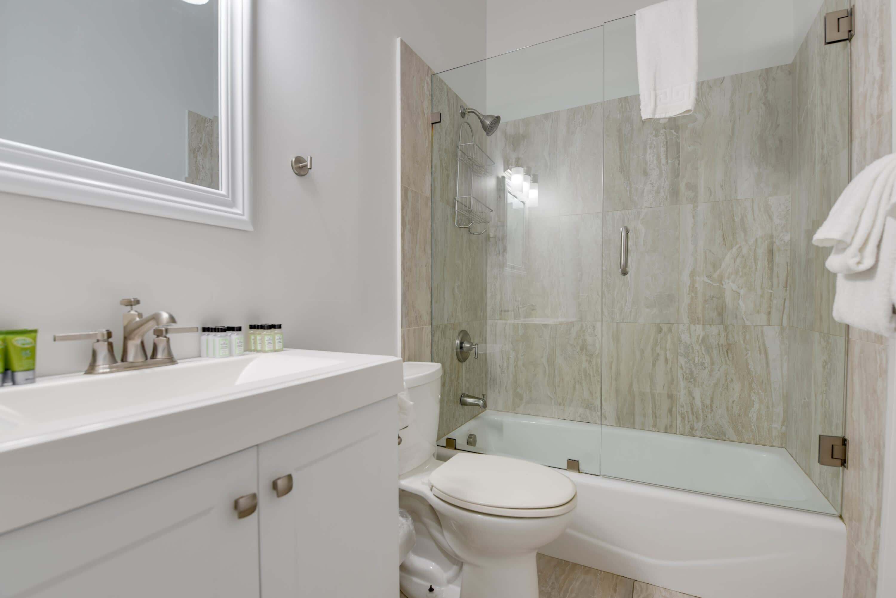 A modern bathroom with a glass-enclosed shower, a white sink with toiletries, and a toilet.
