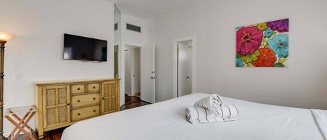 Una habitación de hotel con cama, televisión, un cuadro y ventilador de techo.