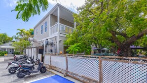 A two-story building with a balcony, a fenced parking area with motorcycles, and a tree in the foreground. - Parking & Shared Pool - Casa Key West (Key West)