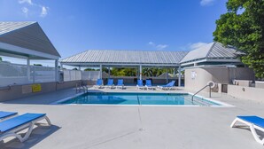 A swimming pool with blue lounge chairs and a covered area with a metal roof. - Parking & Shared Pool - Casa Key West (Key West)