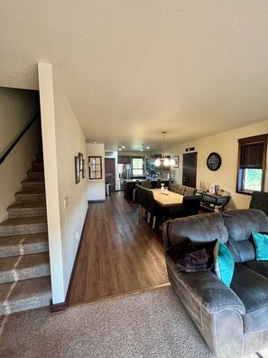 A spacious living area with a staircase, a dining area, and a kitchen in the background.