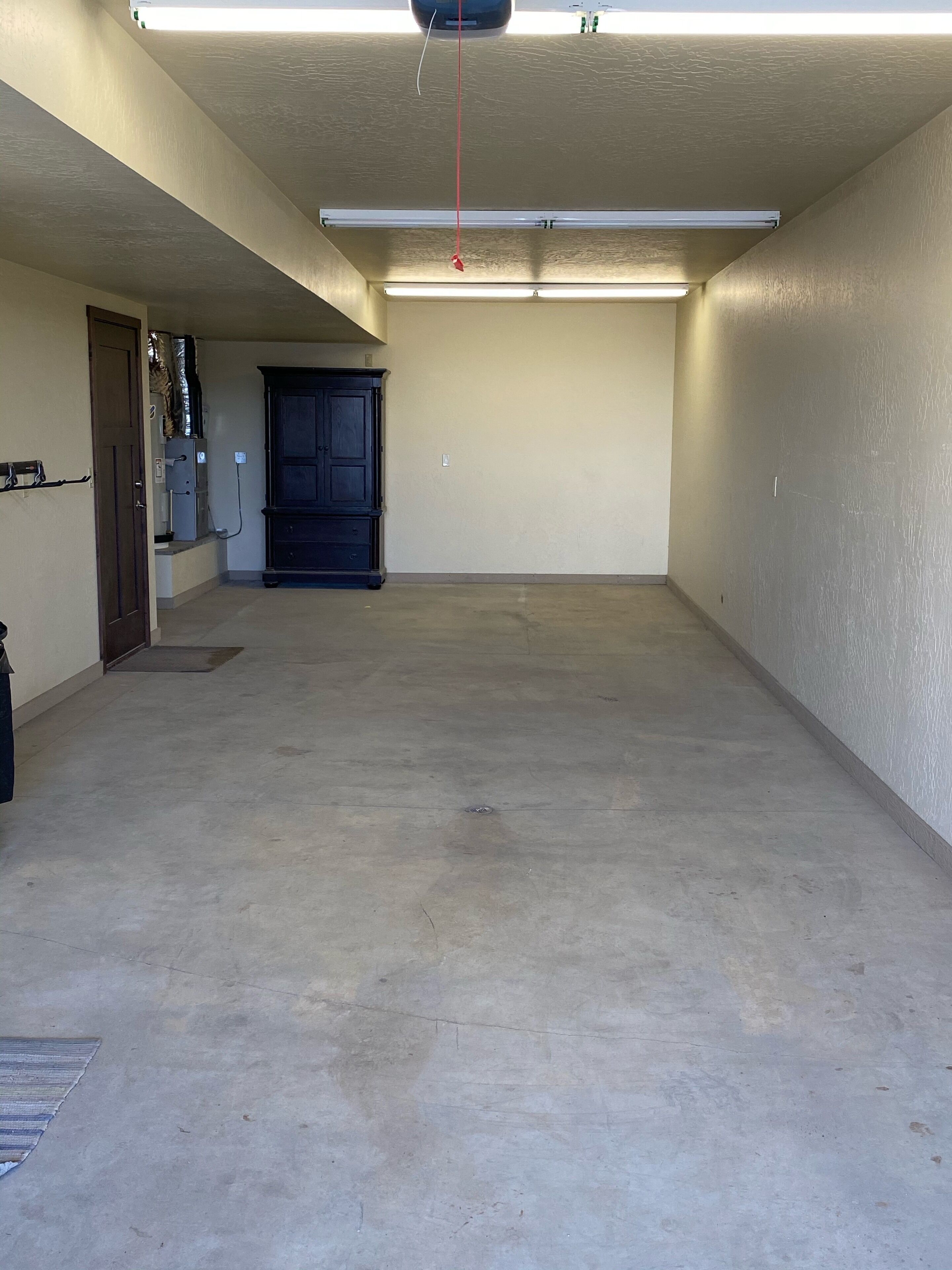 A spacious, empty garage with concrete flooring, a dark wooden cabinet, and a fluorescent light fixture.