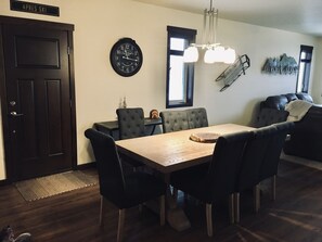 Un comedor con una mesa de madera y sillas tapizadas de color negro, un reloj de pared y una araña.