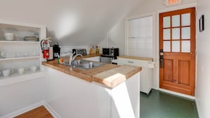 A small kitchen with a sink, a microwave, and a coffee maker. There is a wooden door with an 'EXIT' sign above it. - Traveler's Palm - Studio Near Duval Street (Key West)