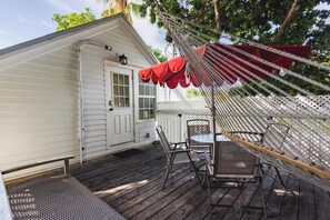A wooden deck with a table and chairs, a white building with a door, and a red canopy. - Traveler's Palm - Studio Near Duval Street (Key West)