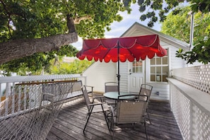 Une terrasse en bois avec un parasol rouge, un hamac et un bâtiment blanc doté d’une porte et de fenêtres.