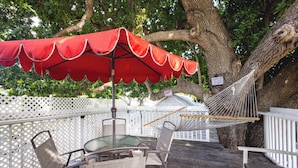 A wooden deck with a table and chairs, a red umbrella, and a hammock. - Traveler's Palm - Studio Near Duval Street (Key West)