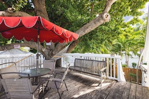 Une terrasse en bois avec une table et des chaises en verre, un parasol rouge et une clôture blanche.