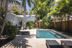 A backyard with a swimming pool, lounge chairs, and a wooden fence. - Coconut Palm - Steps from Duval with Private Pool (Key West)