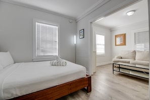 A bedroom with a wooden bed, white bedding, a white sofa, and a glass coffee table. - Coconut Palm - Steps from Duval with Private Pool (Key West)