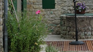 Un edificio de piedra con techo de tejas, puerta verde y una planta en maceta con flores.
