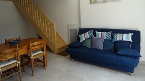 Una sala de estar con una escalera de madera, un sofá azul con cojines estampados y una mesa de comedor con sillas.