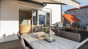 A wooden table with wicker chairs, a lantern, and a coiled rope on a balcony with a glass door leading to an interior space.