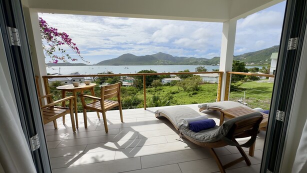 A balcony with a view of a lake and mountains, wooden furniture, and a table with a bowl. - One Bedroom Apartment within walking distance of English Harbour (English Harbour)