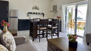 A modern kitchen with dark cabinets, a built-in oven, and a dining area with wooden chairs and a table. - One Bedroom Apartment within walking distance of English Harbour (English Harbour)