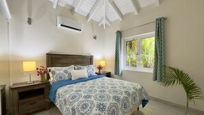 A bedroom with a large bed, two bedside tables, an air conditioning unit, a window with curtains, and a potted plant. - One Bedroom Apartment within walking distance of English Harbour (English Harbour)