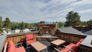 An outdoor patio with stone fireplace, wooden furniture, and a view of the surrounding landscape. - Ridgeview Court Townhome: Incredible Rooftop Deck (Frisco)