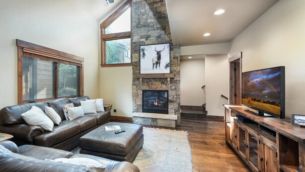 A modern living room with a stone fireplace, leather sofa, and a flat-screen TV. - Ridgeview Court Townhome: Incredible Rooftop Deck (Frisco)