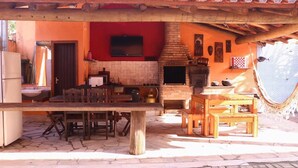 An outdoor kitchen area with a stone floor, wooden furniture, and a brick oven. - Chalés Porto Seguro (São Sebastião)