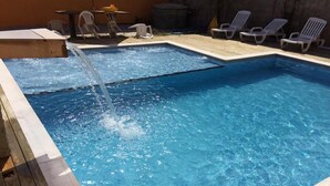 Une piscine rectangulaire à l’eau d’un bleu cristallin, entourée d’une terrasse en bois et de chaises longues blanches.