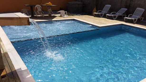 A rectangular swimming pool with clear blue water, surrounded by a wooden deck and white lounge chairs. - Chalés Porto Seguro (São Sebastião)